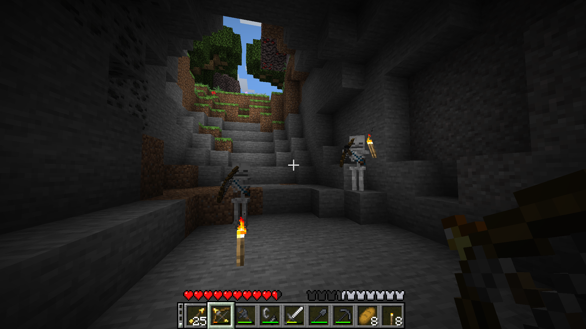 Interior of a shallow cave, with the exit being visible in the distance, light pouring in and some trees and grass are visible. In the cave, the player is battling two skeletons. Two torches light the cave. The player is holding a bow with golden arrows inside, preparing to fight.