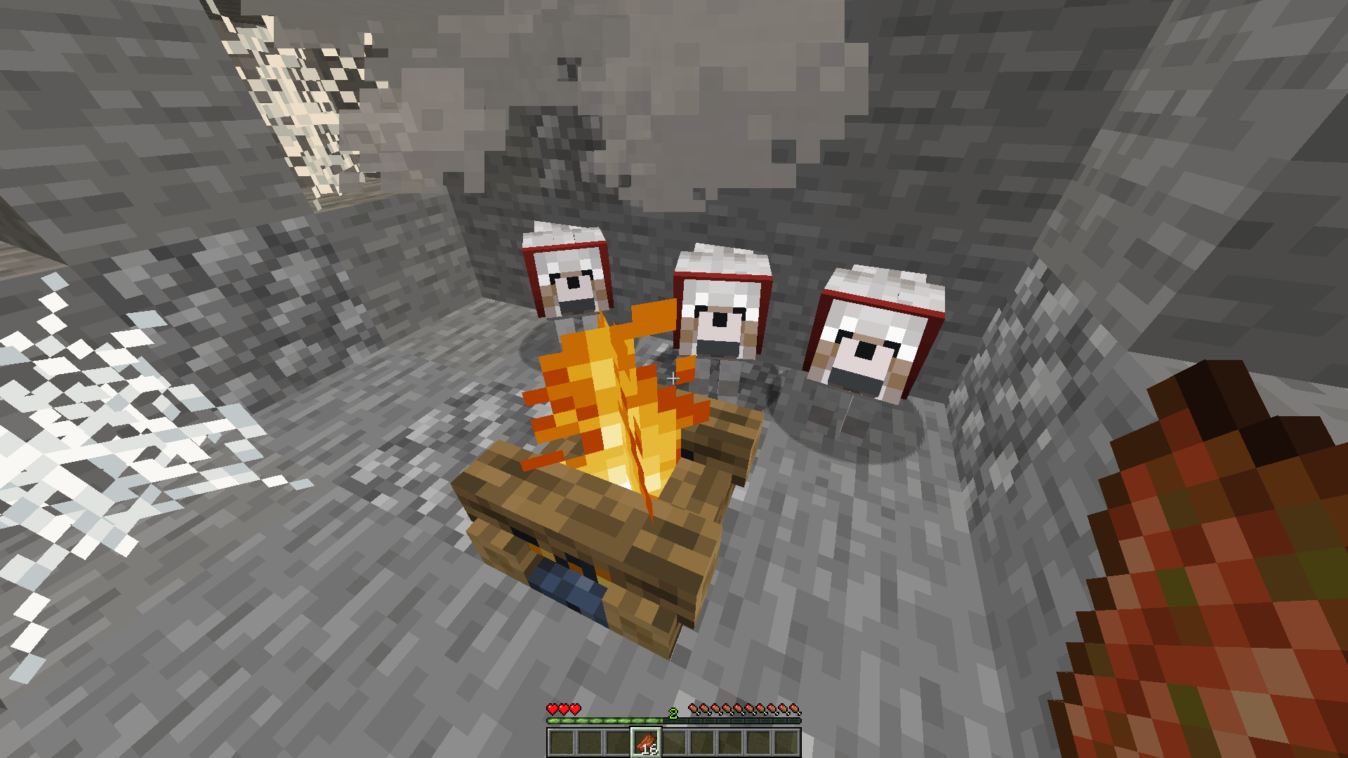 A player sits in a cave near a campfire with three wolves, having only 3 hearts of health left.