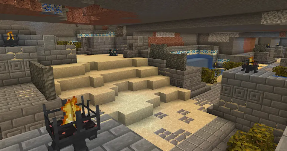 Interior view of a sandy dungeon. Braizers and some plant life growing along water channels can be seen.