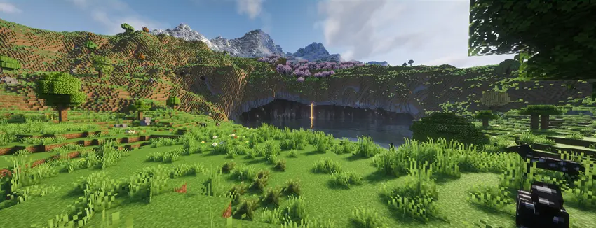 A field of green grass and trees lays before you and in the distance lies beautiful mountainous terrain with a river at the base leading into a cavern that stretches beneath the mountain.